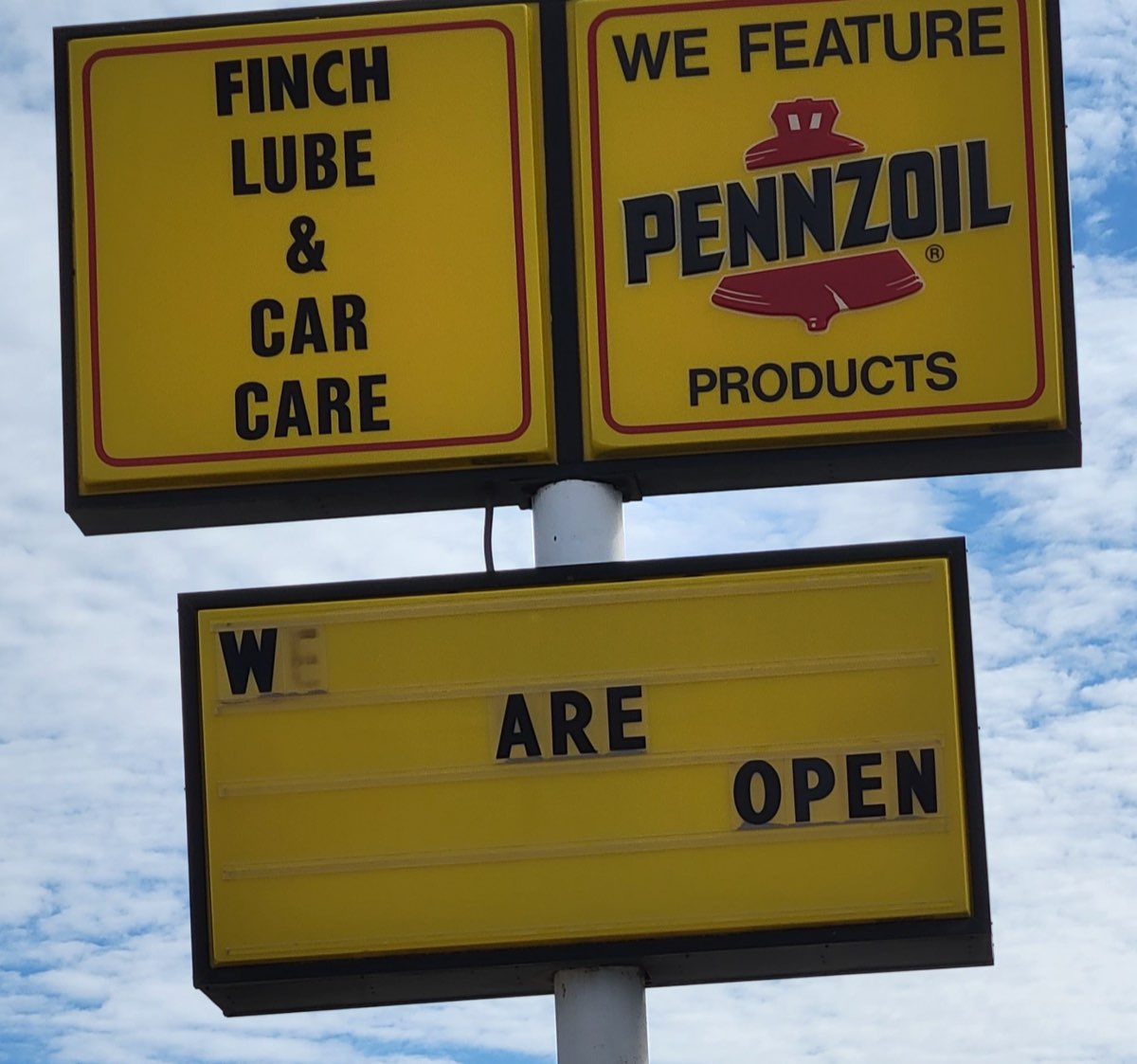 The yellow Finch Lube & Car Care and Pennzoil sign against a blue Farmington sky, reading We Are Open.